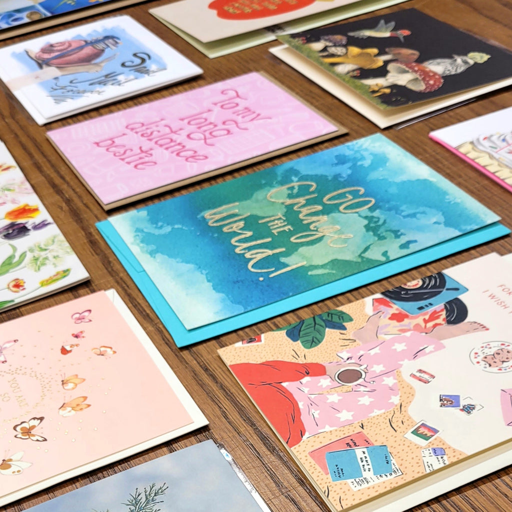 a colourful variety of single greeting cards spread out on a wooden table.